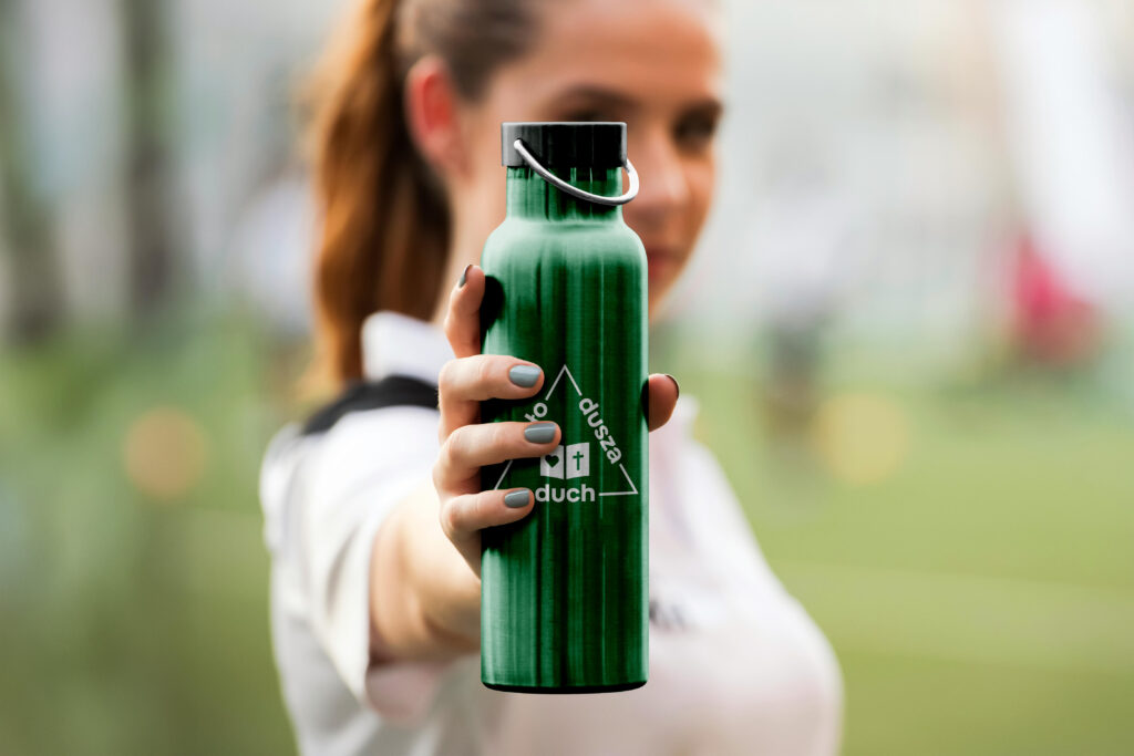 Wizualizacja logo ddc – Logo duch dusza ciało na zielonym termosie ze stali nierdzewnej, trzymanym przez kobietę w koszulce sportowej.